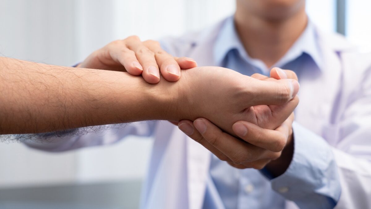 A doctor gently holds a patient&rsquo;s forearm in a reassuring, supportive grip.